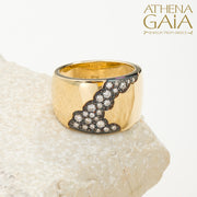 A wide band 18k gold ring with a pattern of inset black and white diamonds along the top side, displayed on a stone surface.