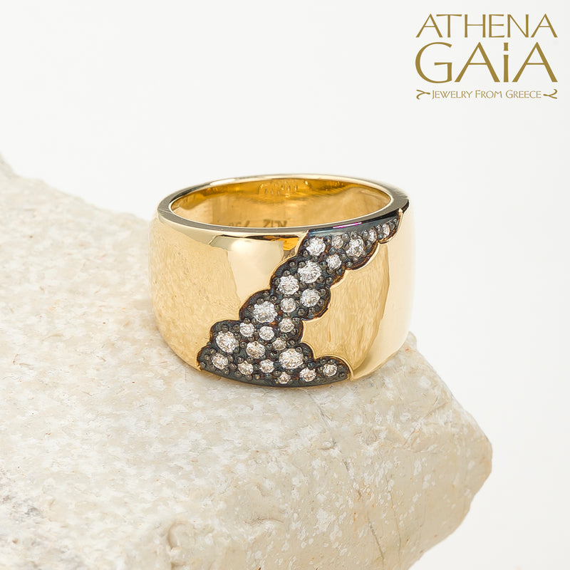 A wide band 18k gold ring with a pattern of inset black and white diamonds along the top side, displayed on a stone surface.