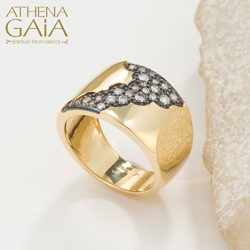 A wide band 18k gold ring with a pattern of inset black and white diamonds along the top side, displayed on a stone surface.