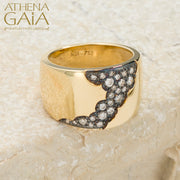 A wide band 18k gold ring with a pattern of inset black and white diamonds along the top side, displayed on a stone surface.