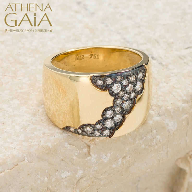 A wide band 18k gold ring with a pattern of inset black and white diamonds along the top side, displayed on a stone surface.