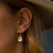 Close-up of an ear wearing a gold earring with a dark background