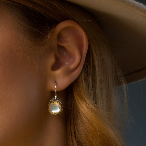Close-up of an ear wearing a gold earring with a dark background