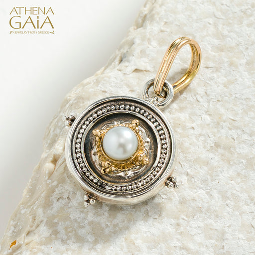 Gold and silver pendant with a pearl on a textured stone background, branded 'Athena Gaia'.