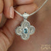 Intricate silver cross pendant with ornate filigree and central blue gemstone held on a silver chain.