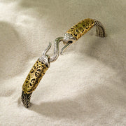 Silver and gold bracelet with ornate filigree and hook clasp, displayed elegantly on fine sand.