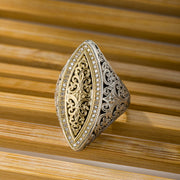 Gold and silver ring with intricate design on a wooden background