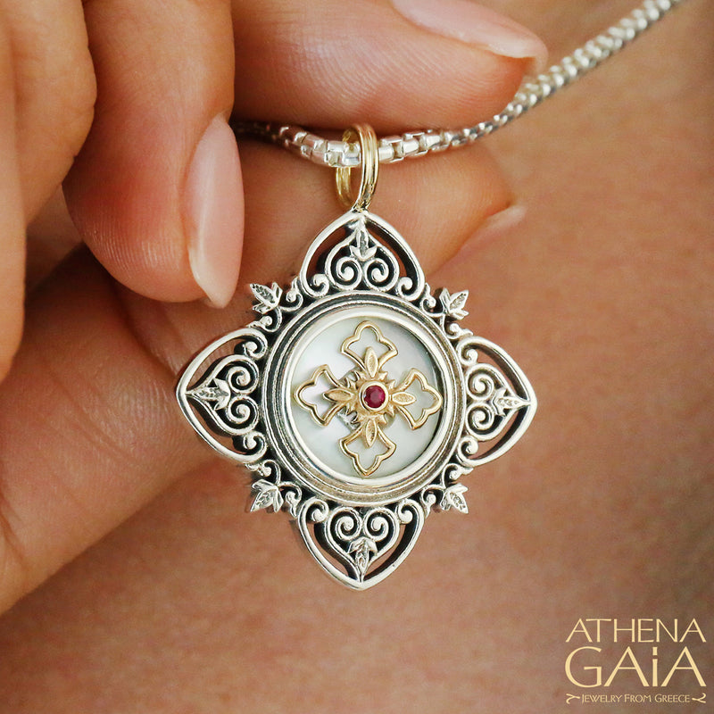 Elegant silver and gold cross pendant with red gemstone center, held by hand on a chain.