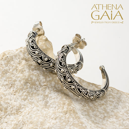 Silver hoop earrings with detailed filigree scrollwork, displayed on a light stone surface.