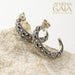 Silver hoop earrings with detailed filigree scrollwork, displayed on a light stone surface.