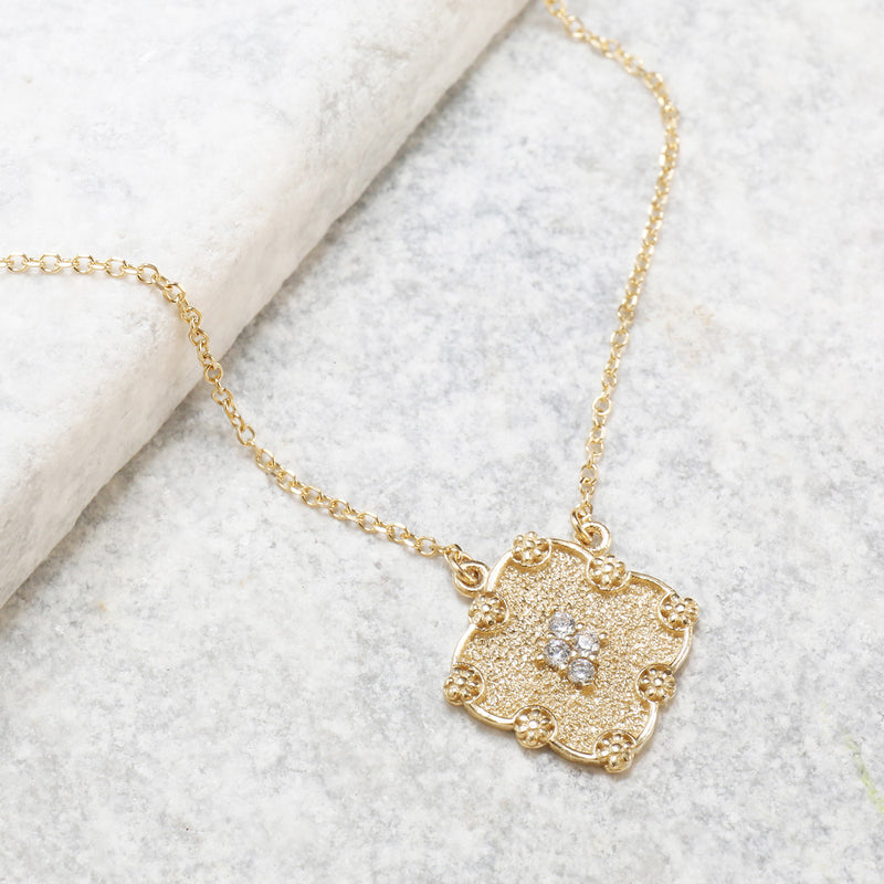 Delicate gold necklace featuring a textured square pendant adorned with small sparkling white stones at its center.