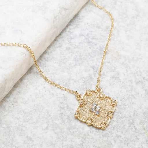 Delicate gold necklace featuring a textured square pendant adorned with small sparkling white stones at its center.