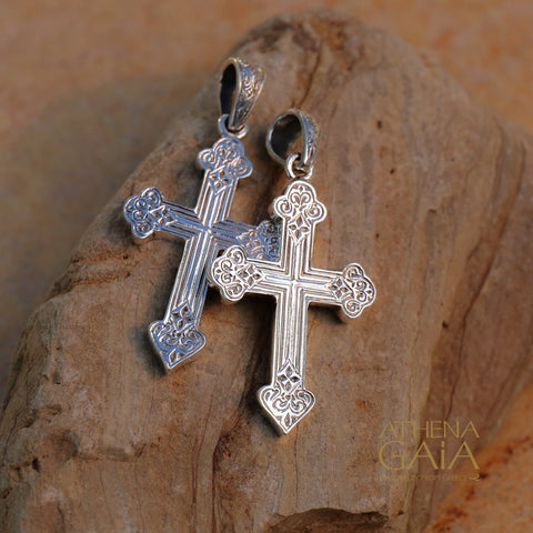 Two ornate sterling silver cross pendants with intricate Greek patterns displayed on a natural stone background.