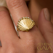 A gold-colored seashell ring with diamond accents, modeled on a human finger.