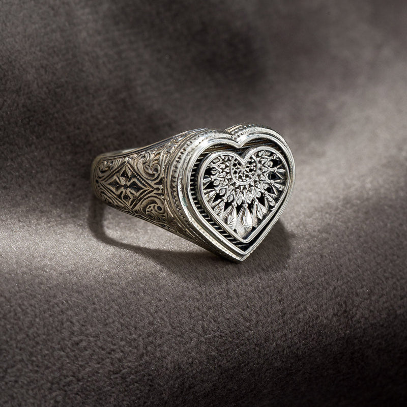 Silver heart-shaped dreamcatcher ring with intricate designs on a dark textured surface