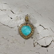 Heart-shaped pendant with a vivid blue stone set in ornate silver and gold detailing against a cracked, textured background