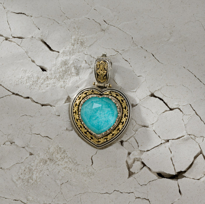 Heart-shaped pendant with a vivid blue stone set in ornate silver and gold detailing against a cracked, textured background