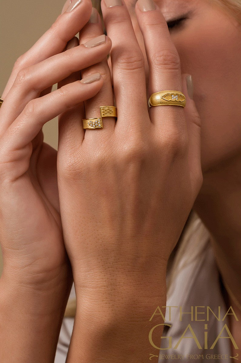 A person wearing two gold rings with intricate geometric designs.