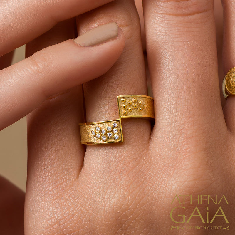 Two hands holding a gold ring with a geometric pattern of diamonds set in it.