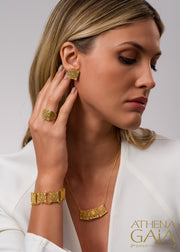 A woman's hand showcasing a gold square grid ring on her finger with the Athena Gaia Jewelry logo visible.