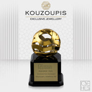 Gold jewelry award on a black base with 'Kouzoupis Exclusive Jewellery' branding.