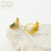 A gold-colored ring with a feathered wing design, displayed on a white rock surface.