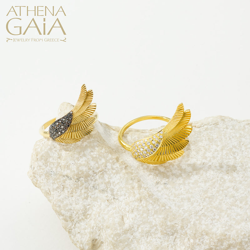 A gold-colored ring with a large wing-like design adorned with small white stones, displayed on a white surface.