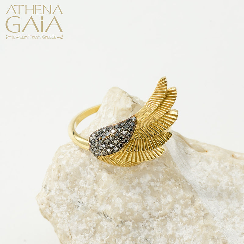 A gold-colored ring with a feathered wing design, displayed on a white rock surface.
