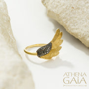 A gold-colored ring with a feathered wing design, displayed on a white rock surface.