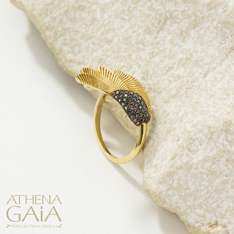 A gold-colored ring with a feathered wing design, displayed on a white rock surface.