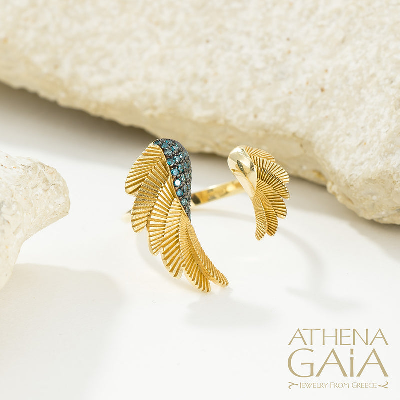 A gold-colored ring with leaf-like designs and blue gemstones placed on a white surface, with the brand name 'ATHENA GAIA' visible.