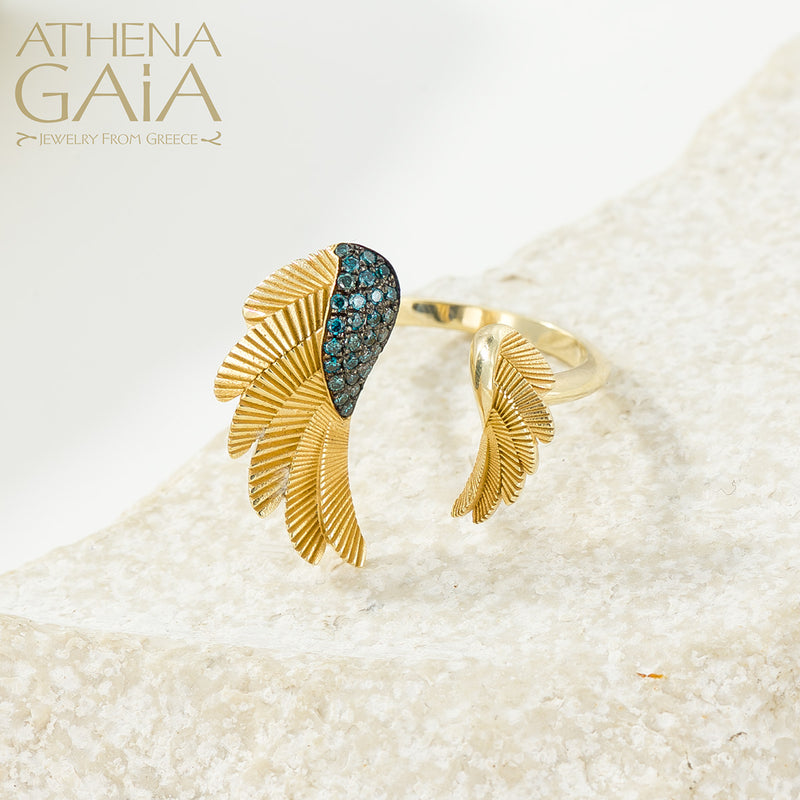 A gold ring with a feathered wing design set with blue gemstones, displayed on a white surface.