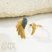 A gold ring with a feathered wing design set with blue gemstones, displayed on a white surface.