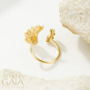 A gold ring with a feathered wing design set with blue gemstones, displayed on a white surface.