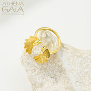 A gold-colored ring with wing-like designs displayed on a textured white surface, with the brand name 'ATHENA GAIA' visible.