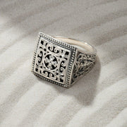 Silver ring with intricate design on sand