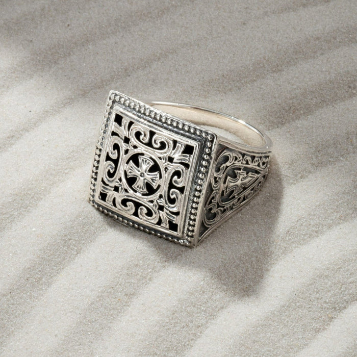 Silver ring with intricate design on sand