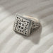 Silver ring with intricate design on sand