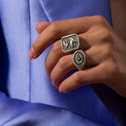 Close-up of a hand wearing two silver rings with intricate designs against a blue fabric background.