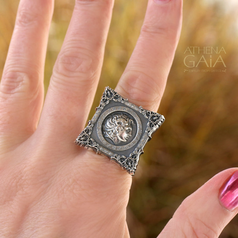 A unisex sterling silver signet ring featuring a profile of Alexander the Great within a decorative frame, displayed on a rock.