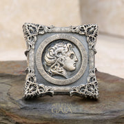 A unisex sterling silver signet ring featuring a profile of Alexander the Great within a decorative frame, displayed on a rock.