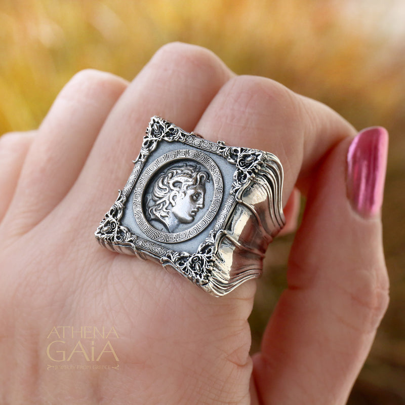 A unisex sterling silver signet ring featuring a profile of Alexander the Great within a decorative frame, displayed on a rock.
