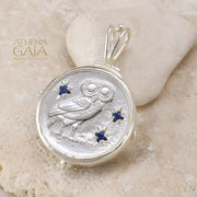 Silver owl pendant with four blue gemstone accents on a stone background.