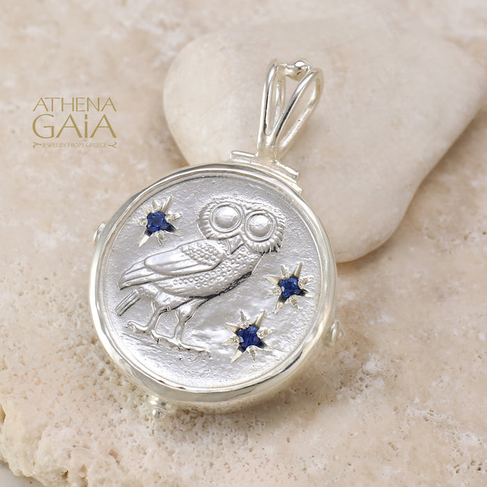 Silver owl pendant with four blue gemstone accents on a stone background.