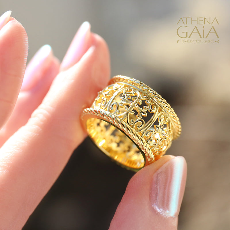 A close-up image of a person's hand wearing a gold ring with intricate embroidery-like detailing, with the brand name 'ATHENA GAIA' visible.