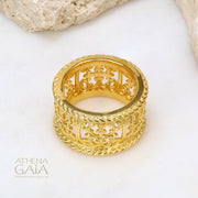 A close-up image of a person's hand wearing a gold ring with intricate embroidery-like detailing, with the brand name 'ATHENA GAIA' visible.