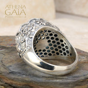 A sterling silver Byzantine filigree ring with a large blue topaz stone, set in a detailed filigree design on a rocky surface.