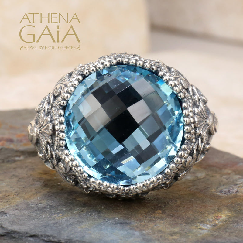 A sterling silver Byzantine filigree ring with a large blue topaz stone, set in a detailed filigree design on a rocky surface.
