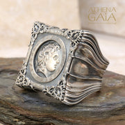 A unisex sterling silver signet ring featuring a profile of Alexander the Great within a decorative frame, displayed on a rock.