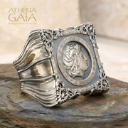 A unisex sterling silver signet ring featuring a profile of Alexander the Great within a decorative frame, displayed on a rock.